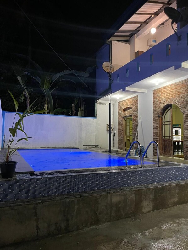 Una piscina con cubierta de baldosas, una antena parabólica y una planta en maceta.
