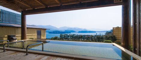 A wooden deck with a glass-bottomed pool overlooking a body of water and mountains.