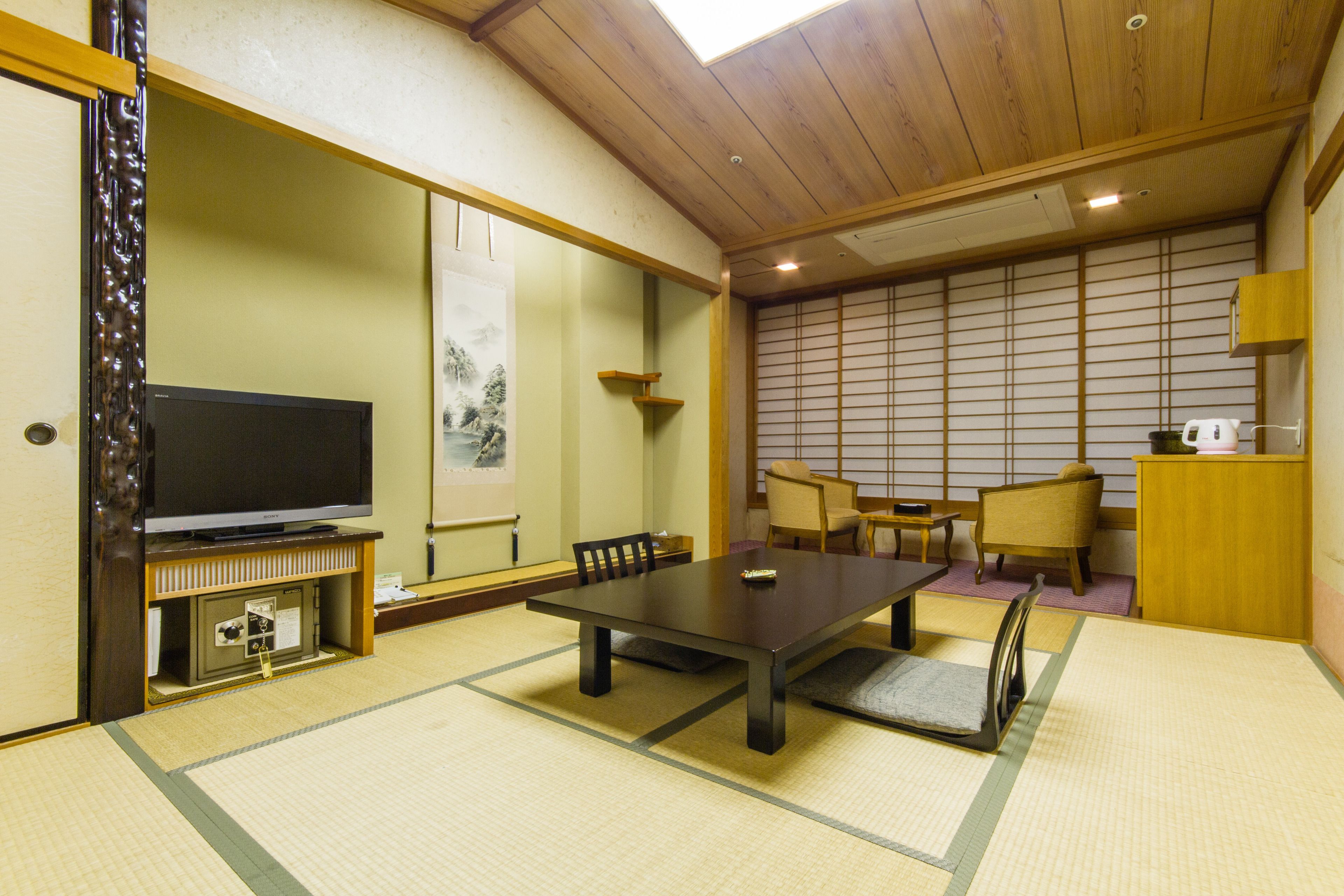 A traditional Japanese room with tatami flooring, a low table, chairs, a television, and sliding doors.