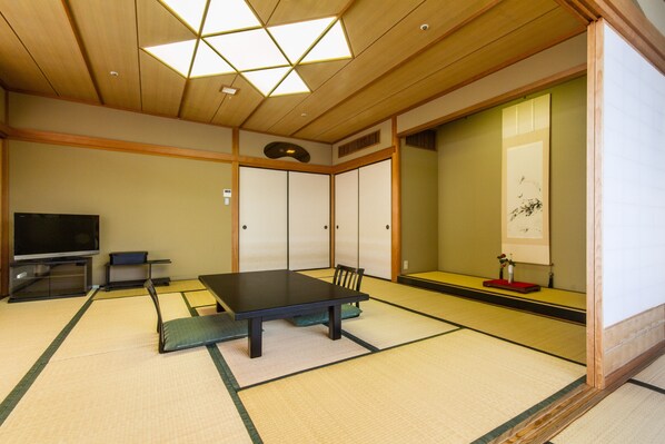 Una habitación japonesa tradicional con suelo de tatami, una mesa baja, un televisor y puertas correderas.