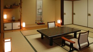 A traditional Japanese room with tatami flooring, a low table, two chairs, a decorative vase, and a sliding door. - Hagi Kanko Hotel (Hagi)