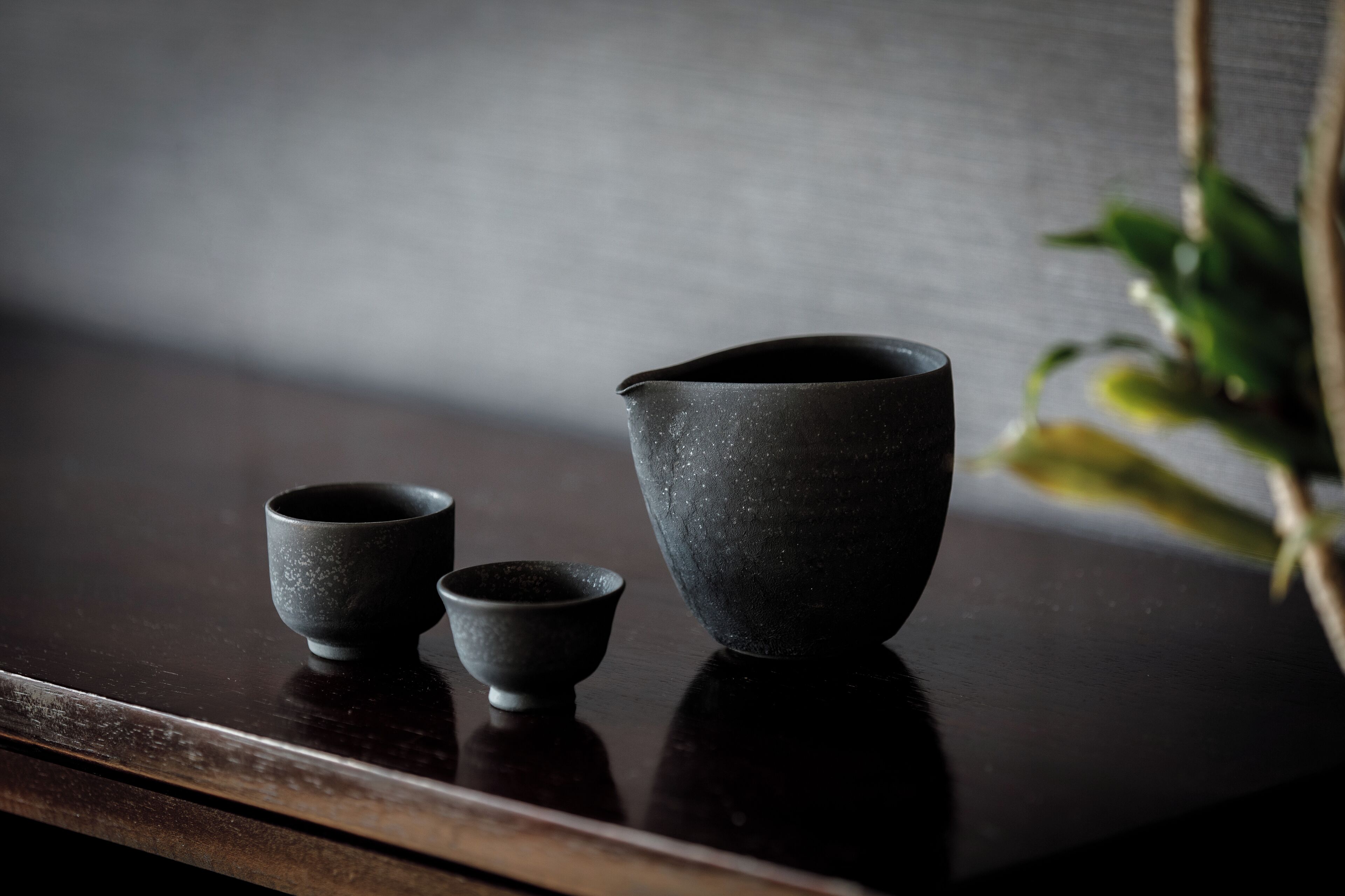 Une table en bois foncé, sur laquelle sont posées trois tasses en céramique et une carafe.
