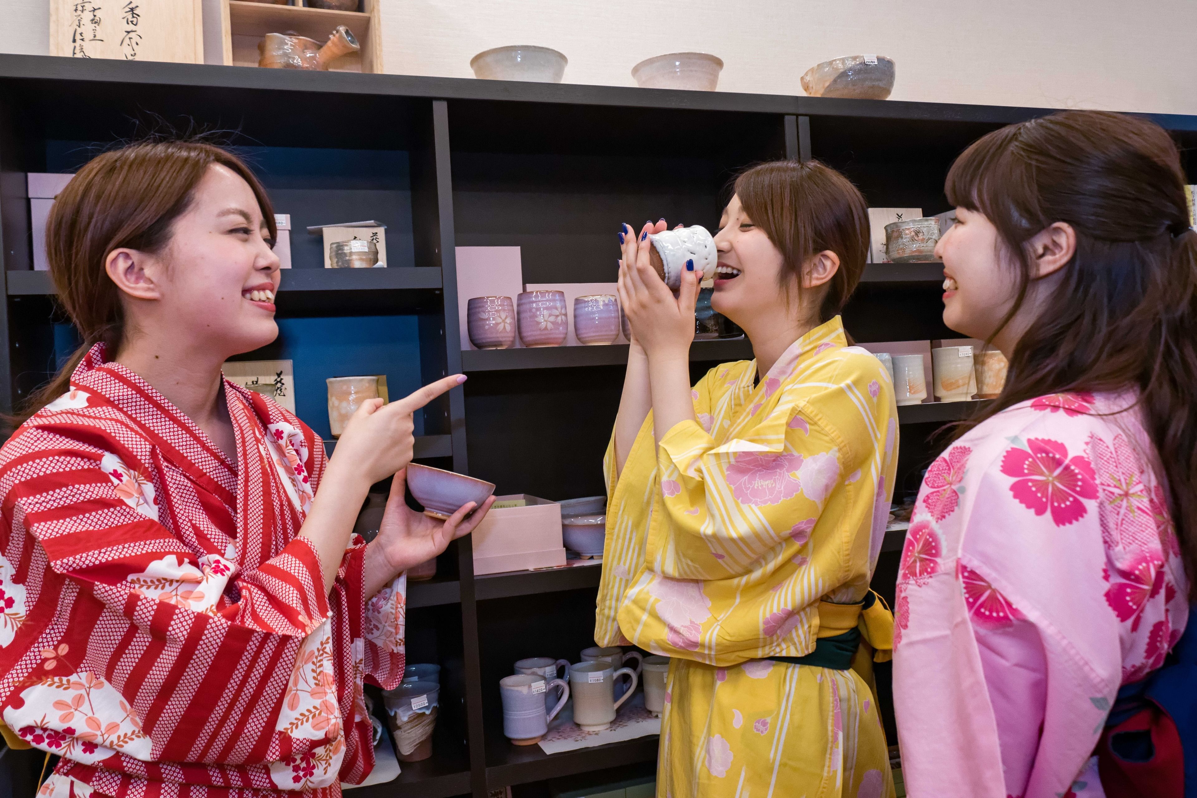 A group of people in traditional attire standing in front of a shelf with various ceramic items.