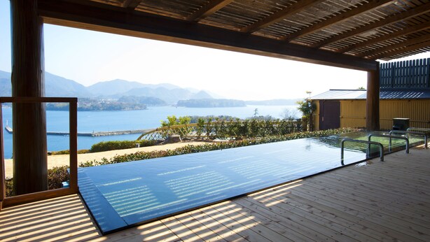 An infinity pool with a view of a lake and mountains, wooden deck, and a covered area with a view. - Hagi Kanko Hotel (Hagi)