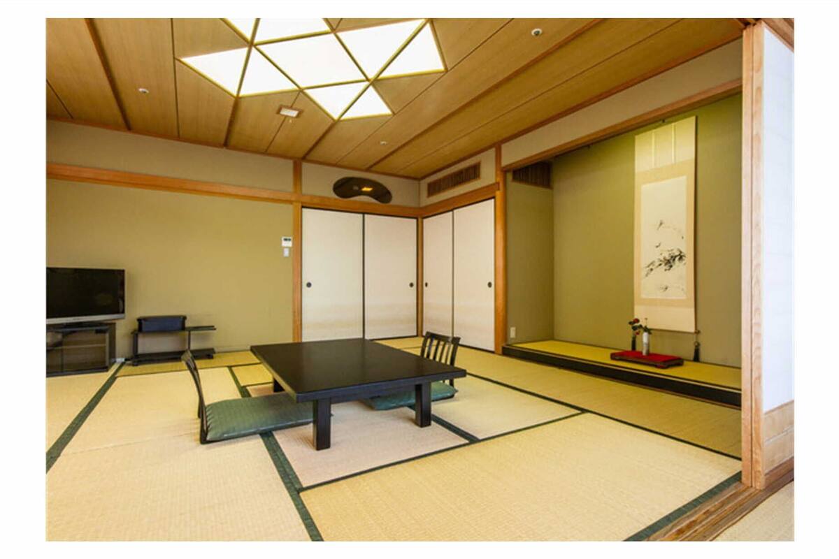 A traditional Japanese room with tatami flooring, a low table, sliding doors, and a television.
