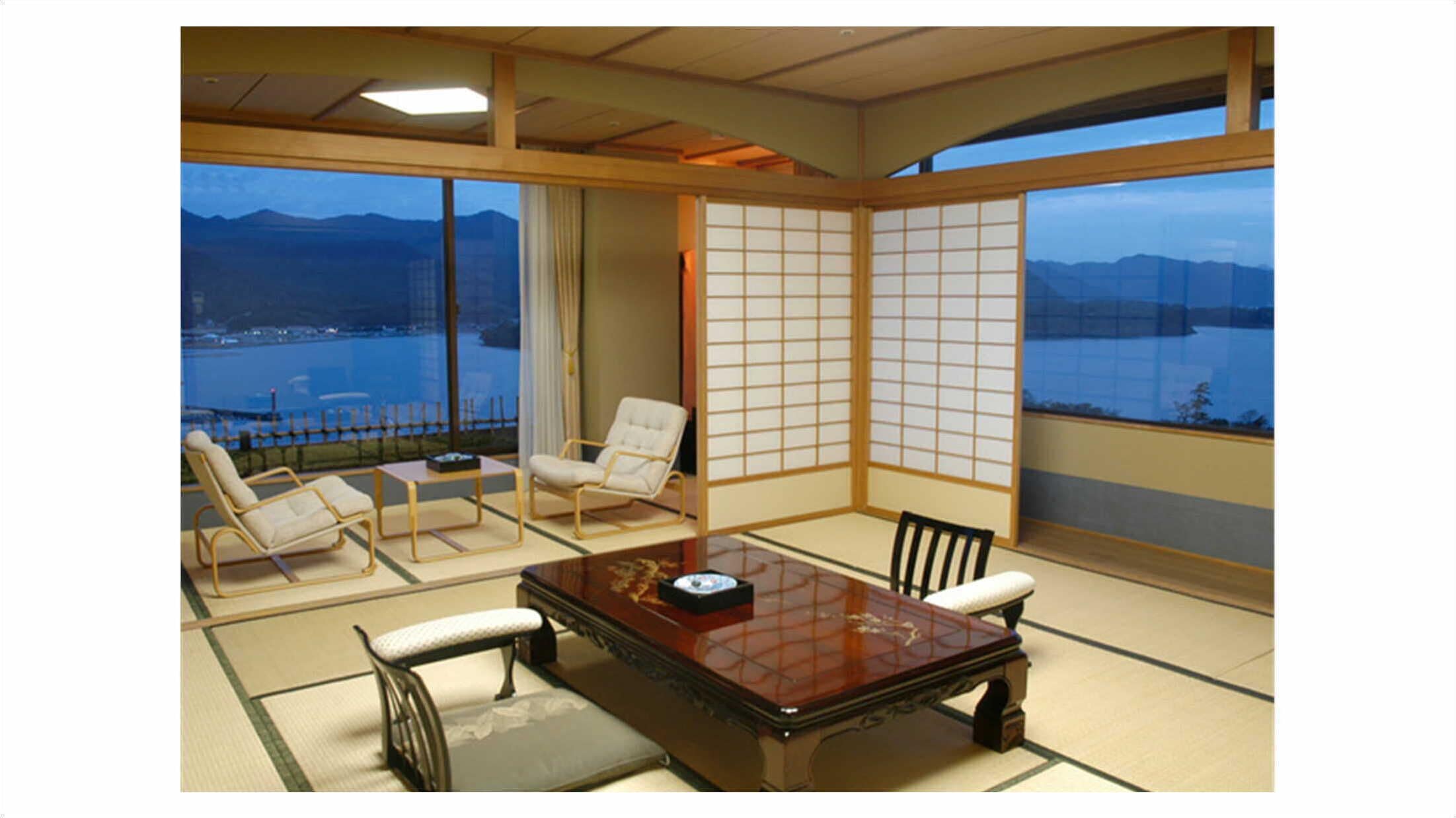 A traditional Japanese room with tatami flooring, a low table, and a view of a body of water and mountains.