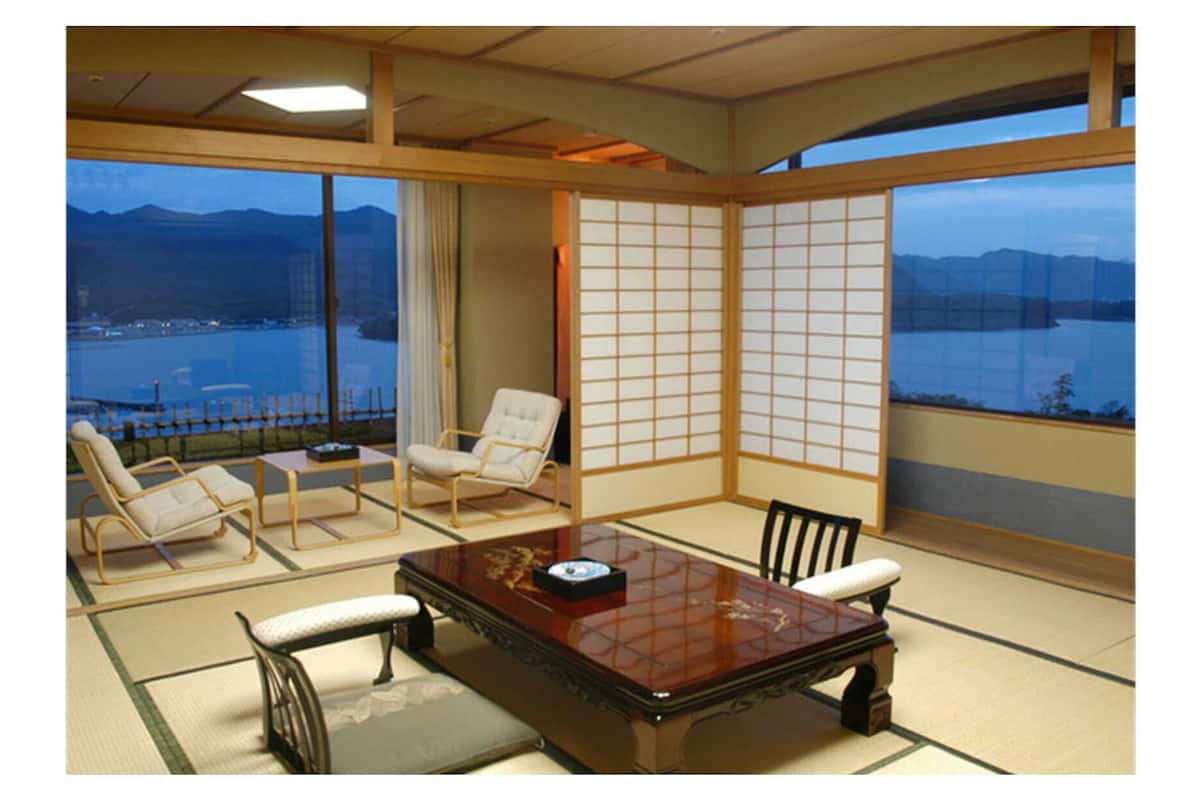 A traditional Japanese room with tatami flooring, a low table, and a view of a body of water and mountains.