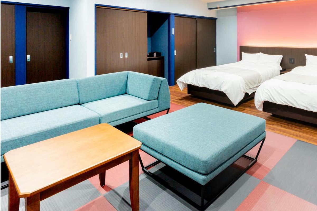 A hotel room with a sofa, two beds, a table, and a wardrobe.