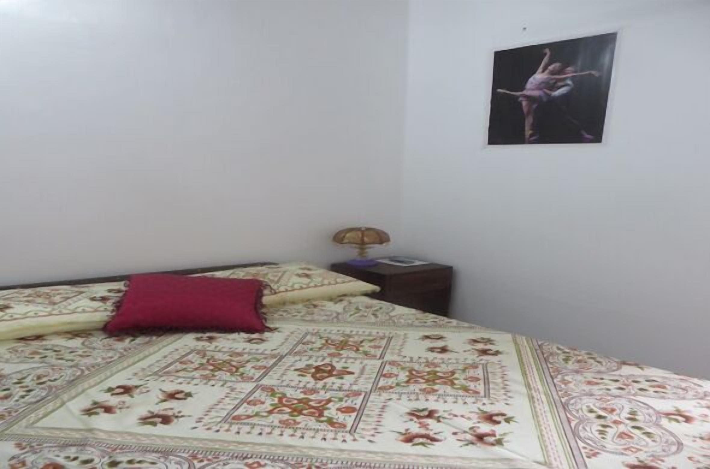 A bedroom with a bed, a nightstand, a lamp, and a poster on the wall.