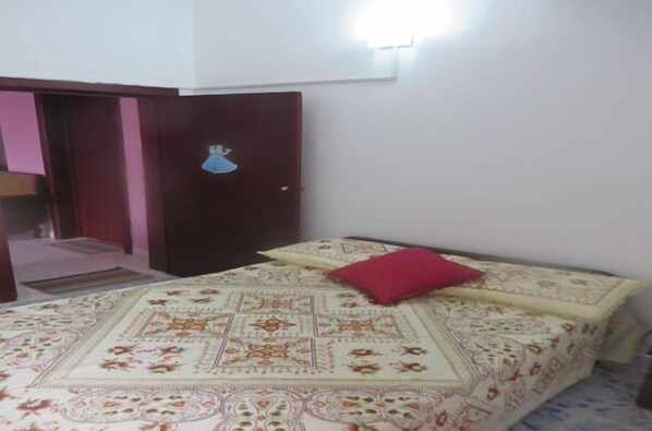 Un dormitorio con una cama, un almohadón rojo y una puerta con interruptor de luz.