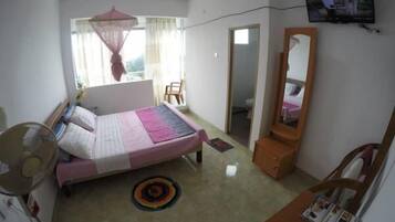 Un dormitorio con cama, mesita de noche, espejo, televisor y ventana con cortinas.