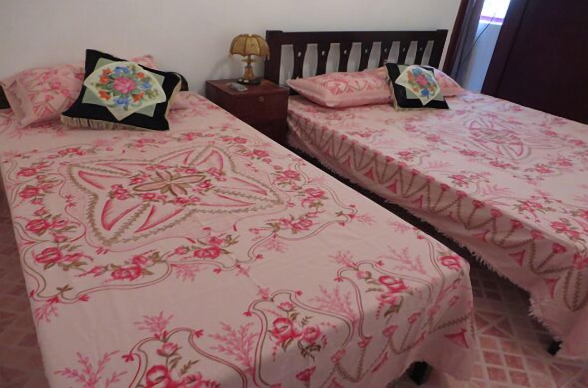 Una habitación con dos camas, cada una con ropa de cama de estampado floral y almohadas a juego. Entre las camas, se encuentra una mesita de noche con una lámpara.