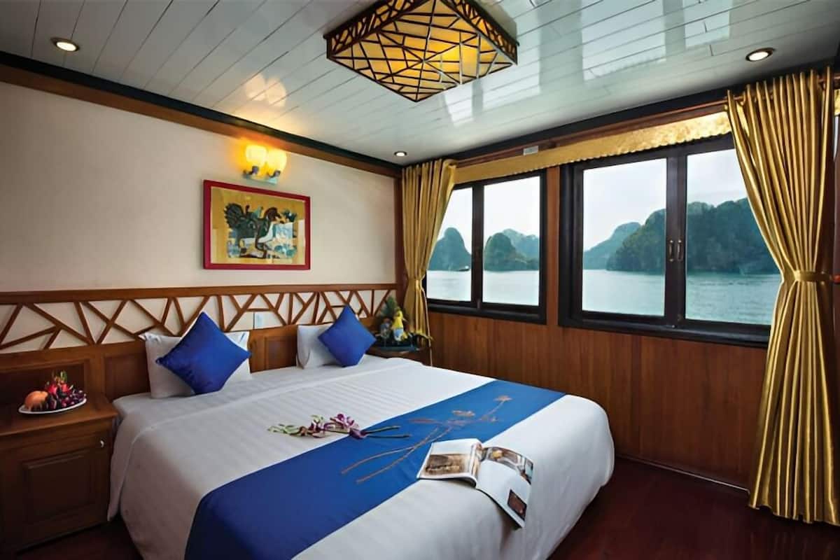 Un cuarto de hotel con una cama grande, un cabecero de madera, un cuadro en la pared y una ventana con vista al agua.