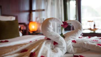 A bed with a white blanket and rose petals, a swan-shaped towel, and a rose.