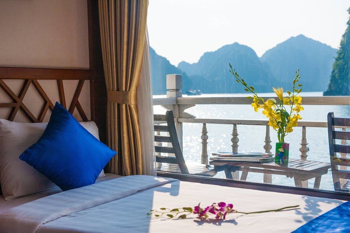 Un balcón con una cama, un jarrón con flores amarillas y vistas a montañas y agua.