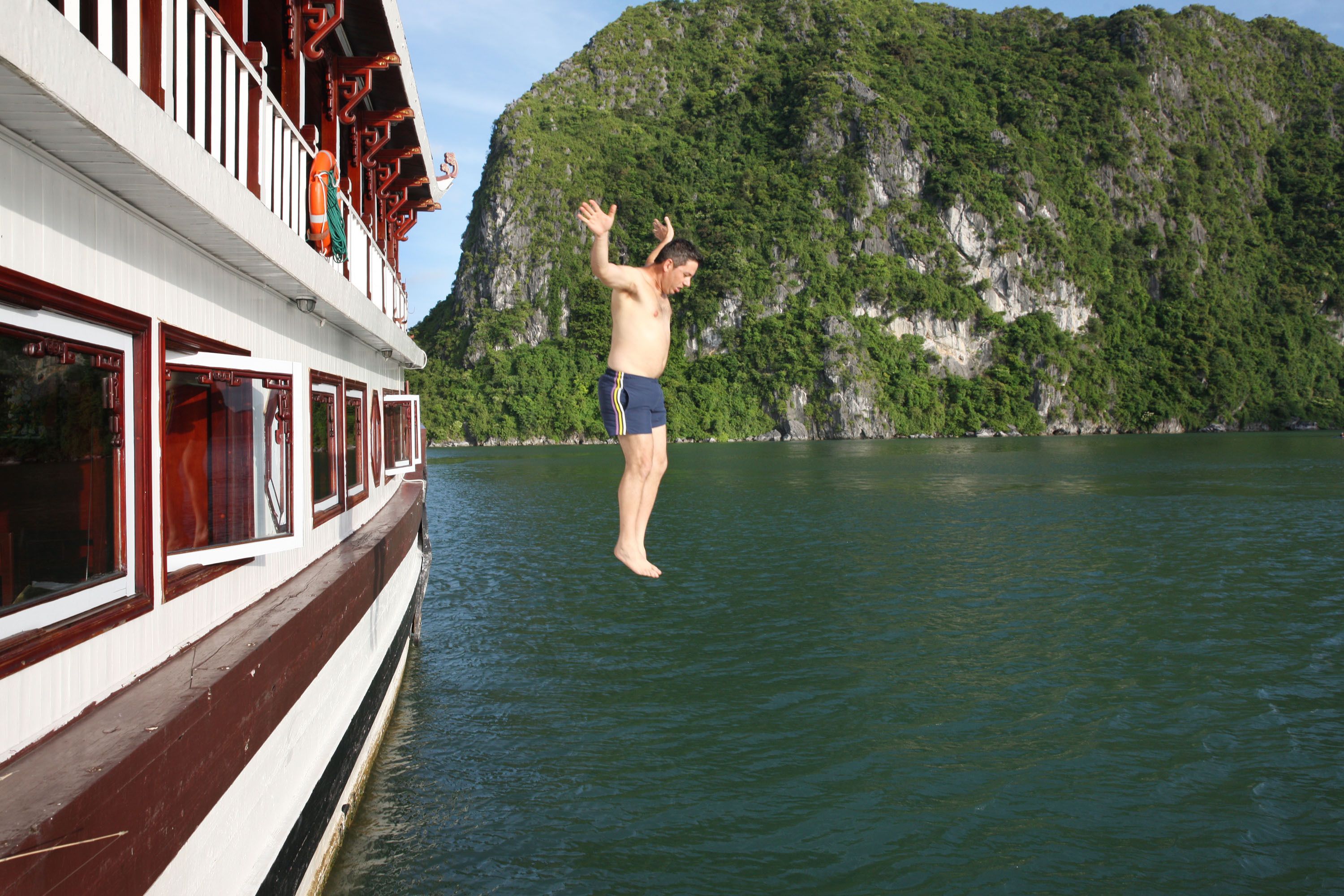 A man jumping off a boat into a body of water with a mountainous landscape in the background.