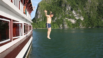 A man jumping off a boat into a body of water with a mountainous landscape in the background.