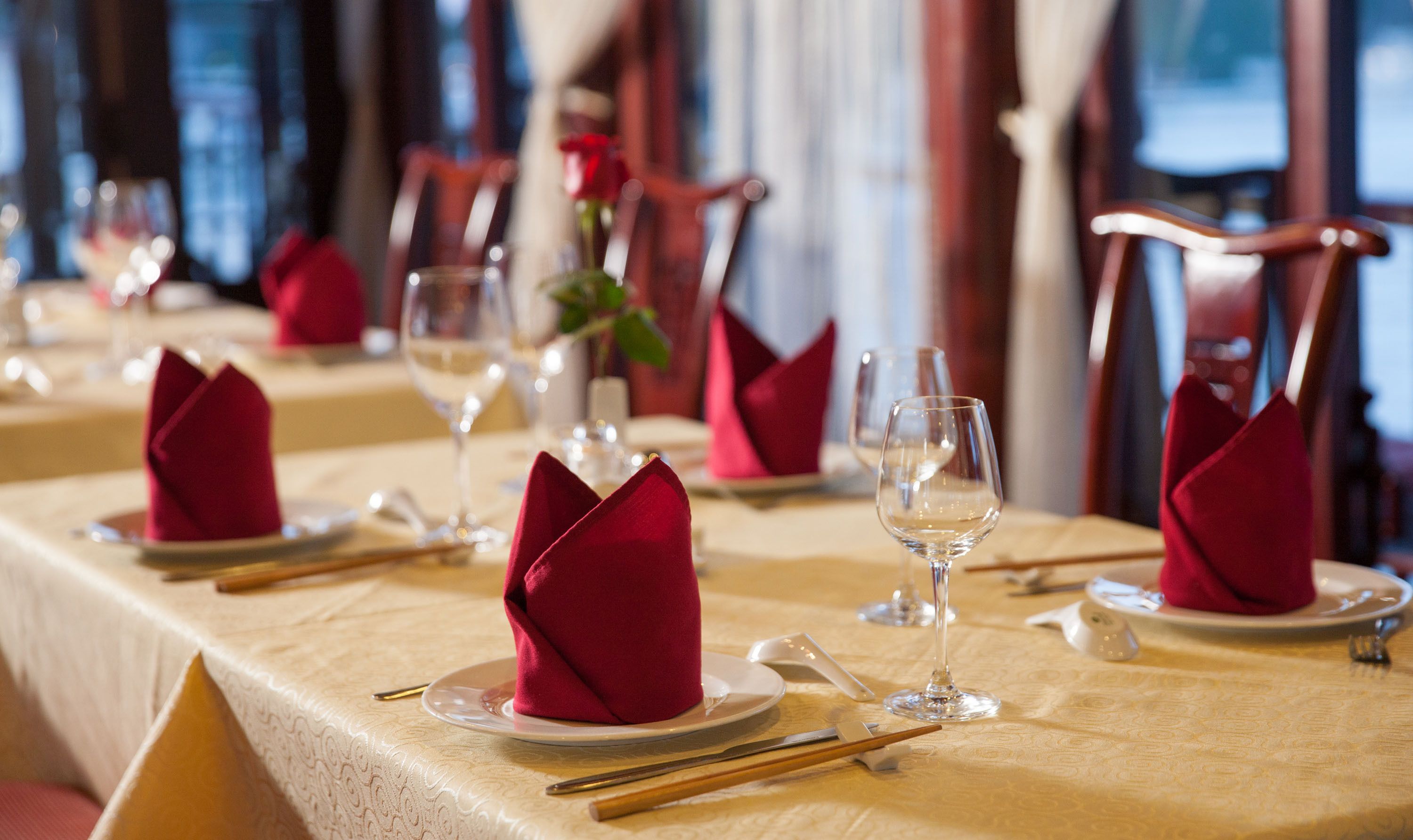 A dining table set with red napkins, wine glasses, and chopsticks.
