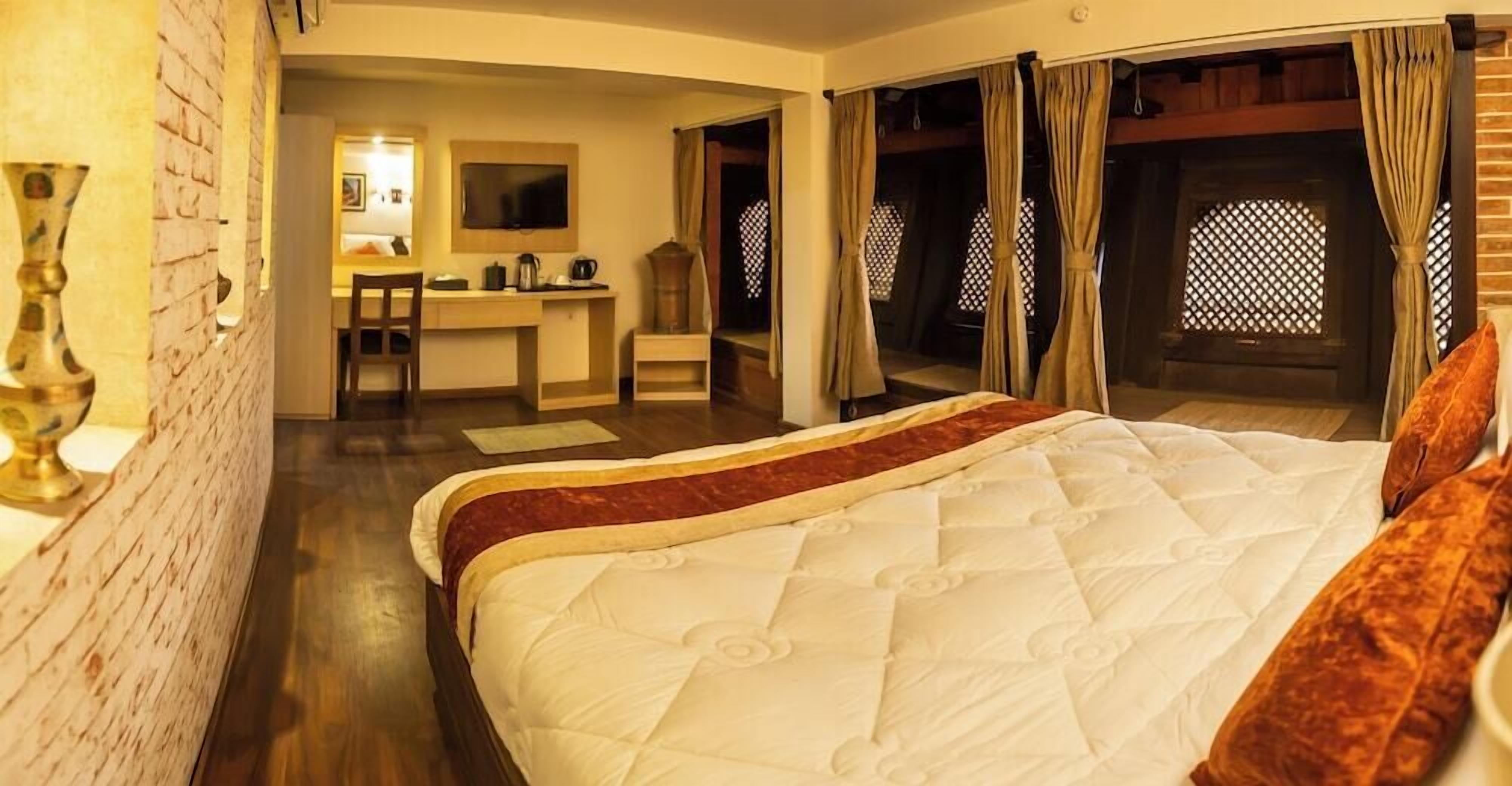A bedroom with a large bed, a desk, and a chair. There are curtains and a window with a lattice design.