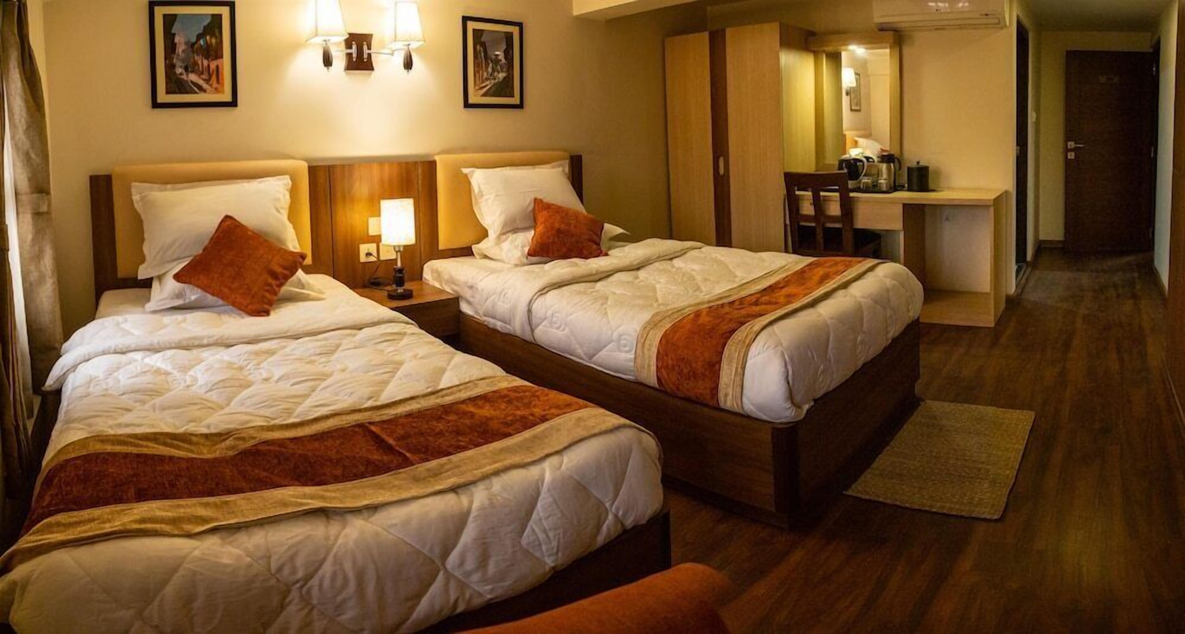 A hotel room with two beds, a desk, and a chair.
