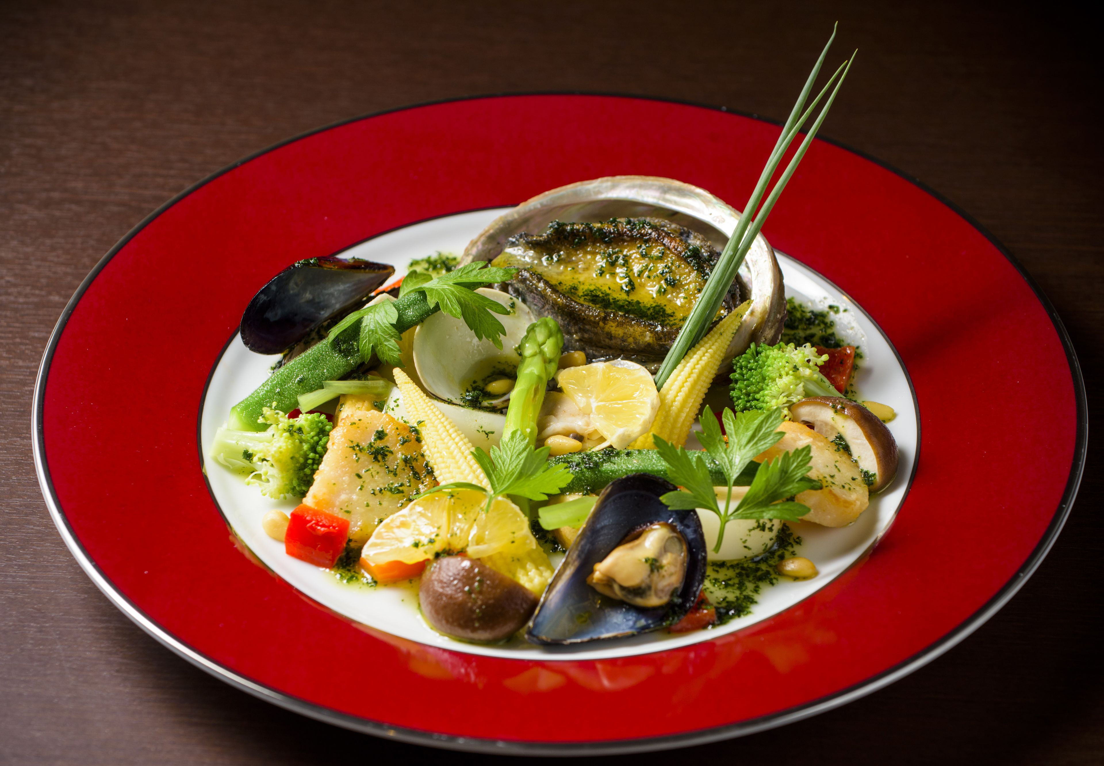 A seafood dish with mussels, corn, and vegetables on a red plate.