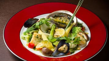 A seafood dish with mussels, corn, and vegetables on a red plate.