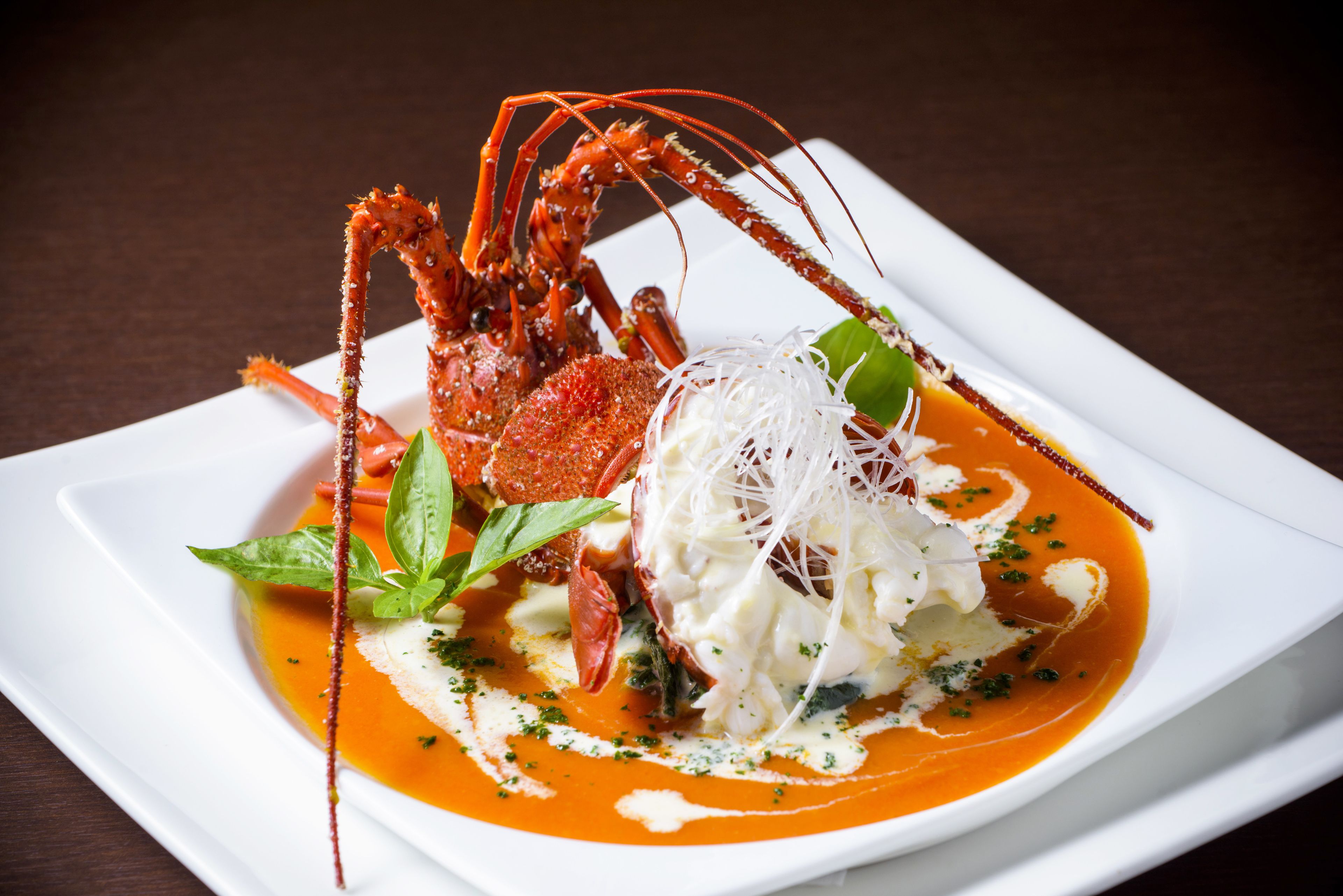 A lobster dish with a white plate, garnished with basil and a creamy sauce.