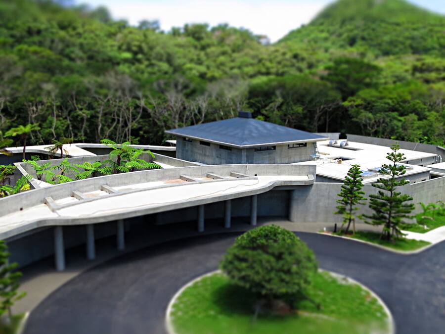 A model of a modern building with a curved roof, surrounded by greenery and a landscaped area.