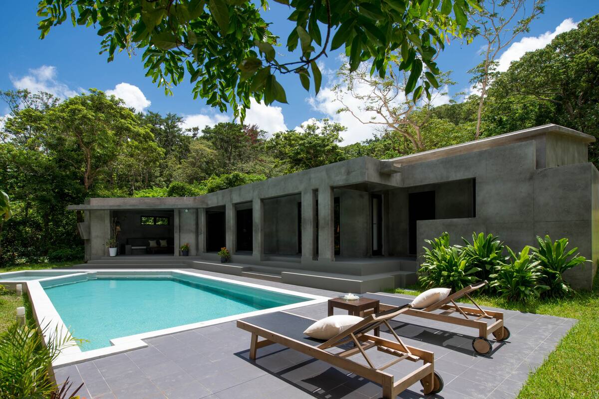A modern house with a swimming pool, outdoor seating, and lush greenery.