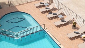 Piscina com escadas revestidas em azulejo e espreguiçadeiras com guarda-sóis.