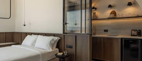 Une chambre d’hôtel moderne équipée d’un lit, d’une table de chevet et d’un coin cuisine avec un réfrigérateur et un plan de travail.