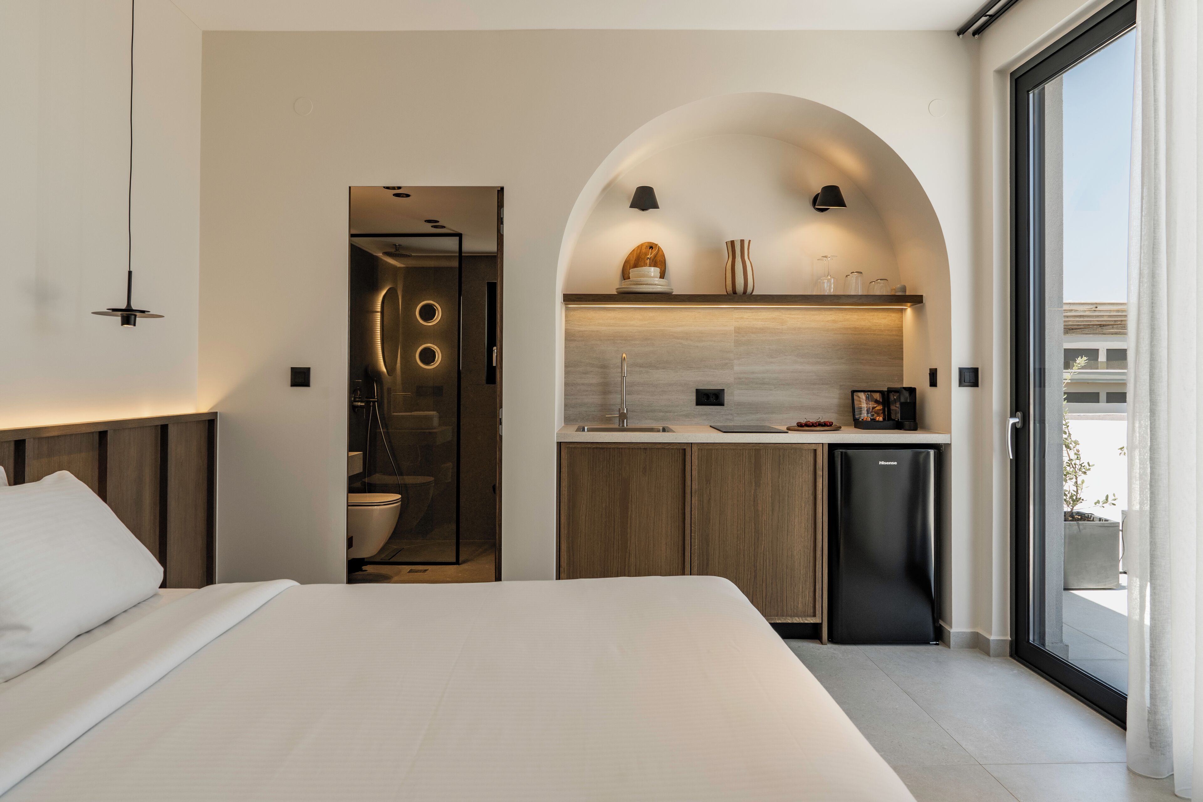 A modern bedroom with a large bed, a built-in desk, and a kitchen area with a sink and a refrigerator.