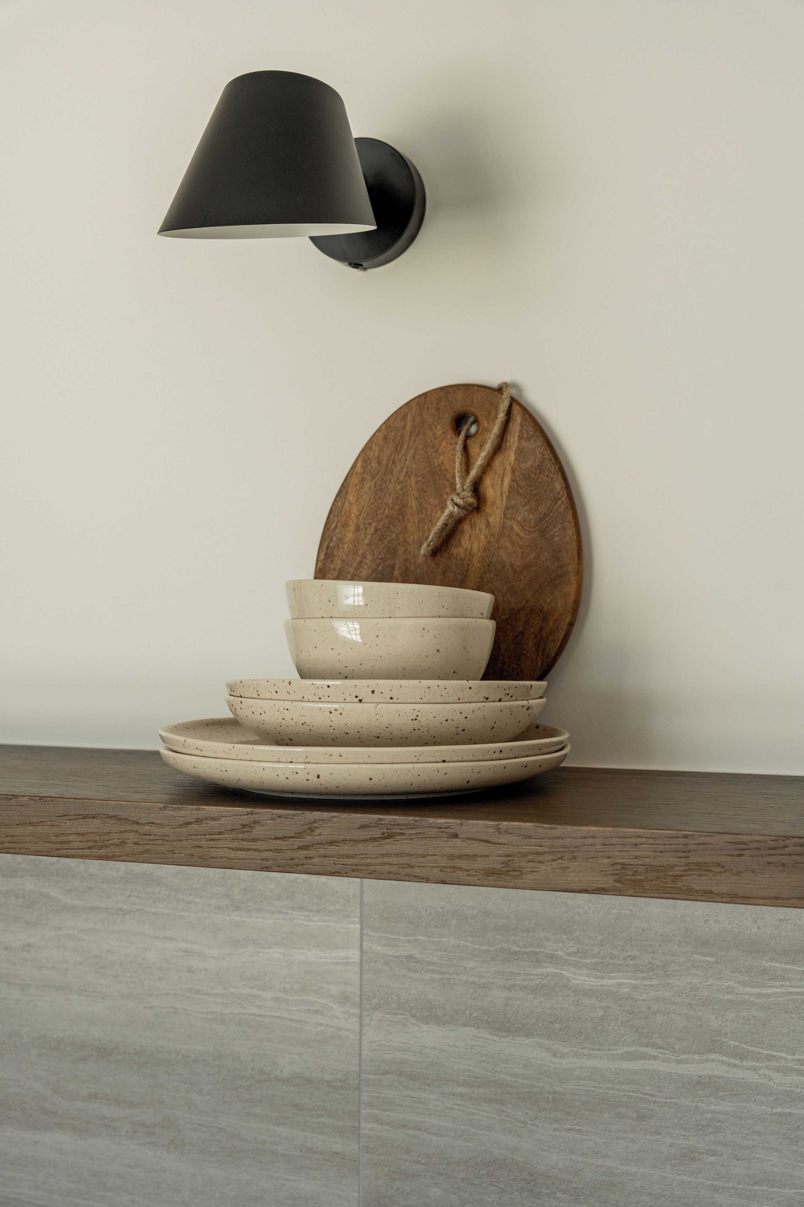 Una lámpara de pared, una tabla de madera con una cuerda, y cuencos apilados sobre una mesa.