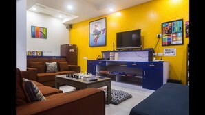 A living room with a sofa, a coffee table with chess, a TV, and a blue cabinet. - Joey's Hostel (New Delhi)