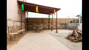 An outdoor patio with tiled flooring, a covered seating area with chairs, and a table. - Joey's Hostel (New Delhi)