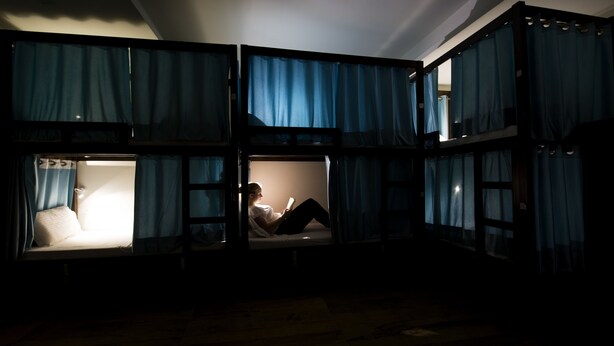 A dormitory-style room with bunk beds, a small table, and a reading light. - Joey's Hostel (New Delhi)
