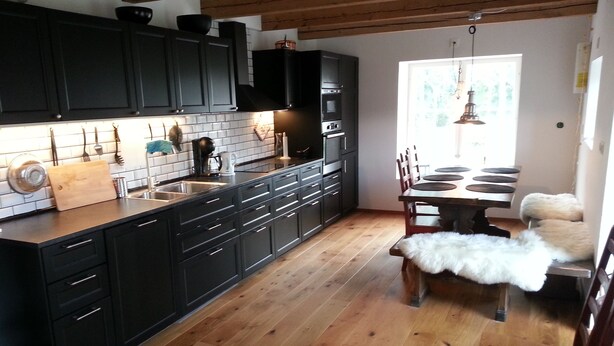 Een moderne keuken met donkere kastjes, een houten aanrecht en een eethoek met een tafel en stoelen.