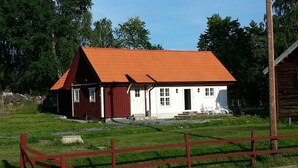 A small, single-story house with a red roof and white walls, surrounded by a fenced yard and trees. - Abborrtorps Gård (Arboga)