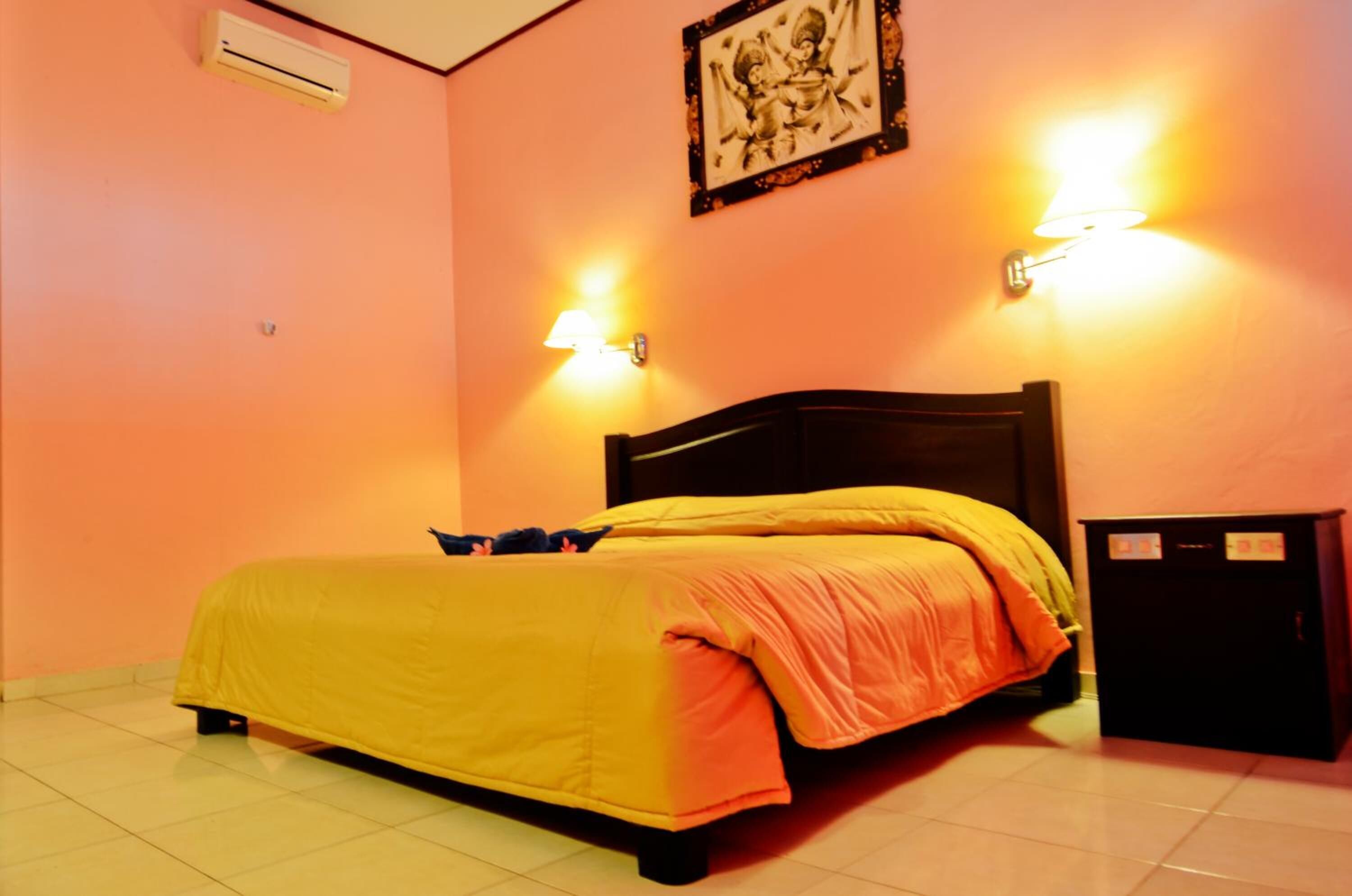 A room with a bed, two wall-mounted lamps, a framed picture, and a small cabinet.