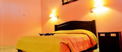 A room with a bed, two wall-mounted lamps, a framed picture, and a small cabinet.