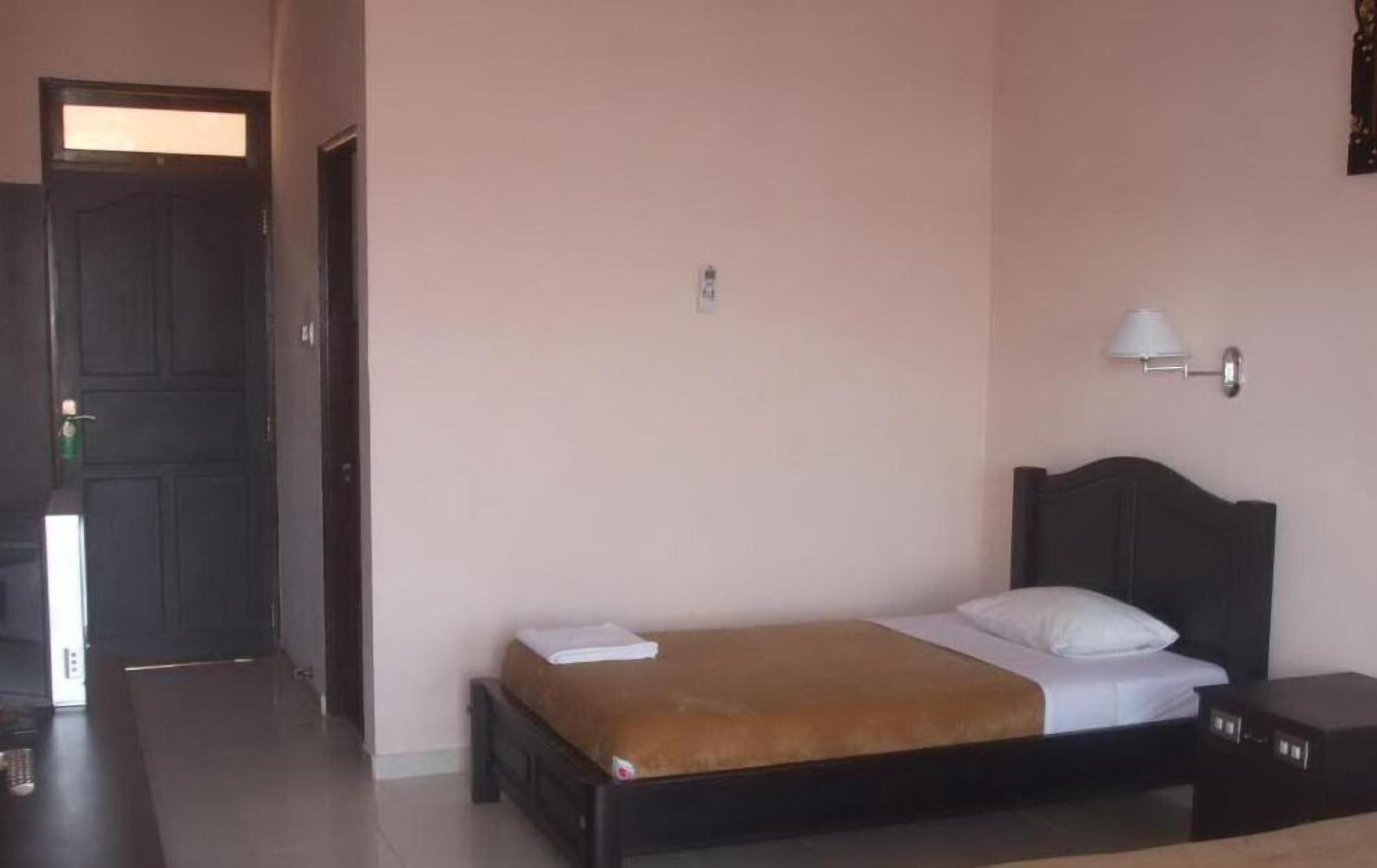 A bedroom with a bed, bedside tables, a door, and a wall-mounted lamp.