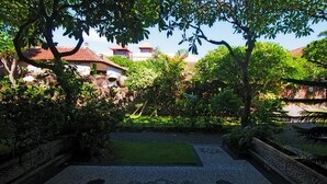A courtyard with a patterned stone floor, surrounded by lush greenery and a small lawn. - Pesona Beach Inn (Kuta)
