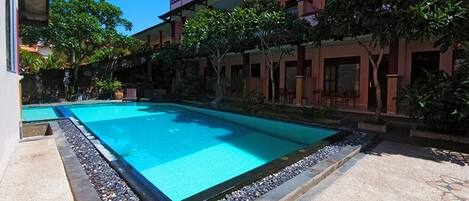 A swimming pool surrounded by a building with multiple balconies and trees.