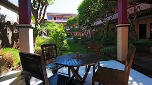 An outdoor patio area with a round table and four chairs, surrounded by lush greenery and a view of a building in the background. - Pesona Beach Inn (Kuta)