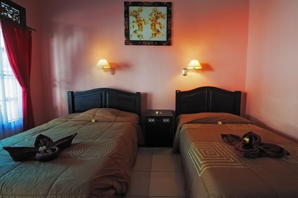 Habitación de hotel con dos camas, cada una con cabecera, una mesita de noche entre ellas y una lámpara de pared.