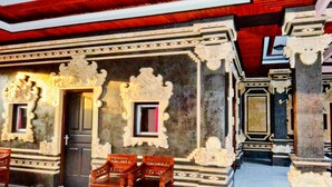An ornate room with carved walls, a wooden bench, and a door with a mirror. - Pesona Beach Inn (Kuta)