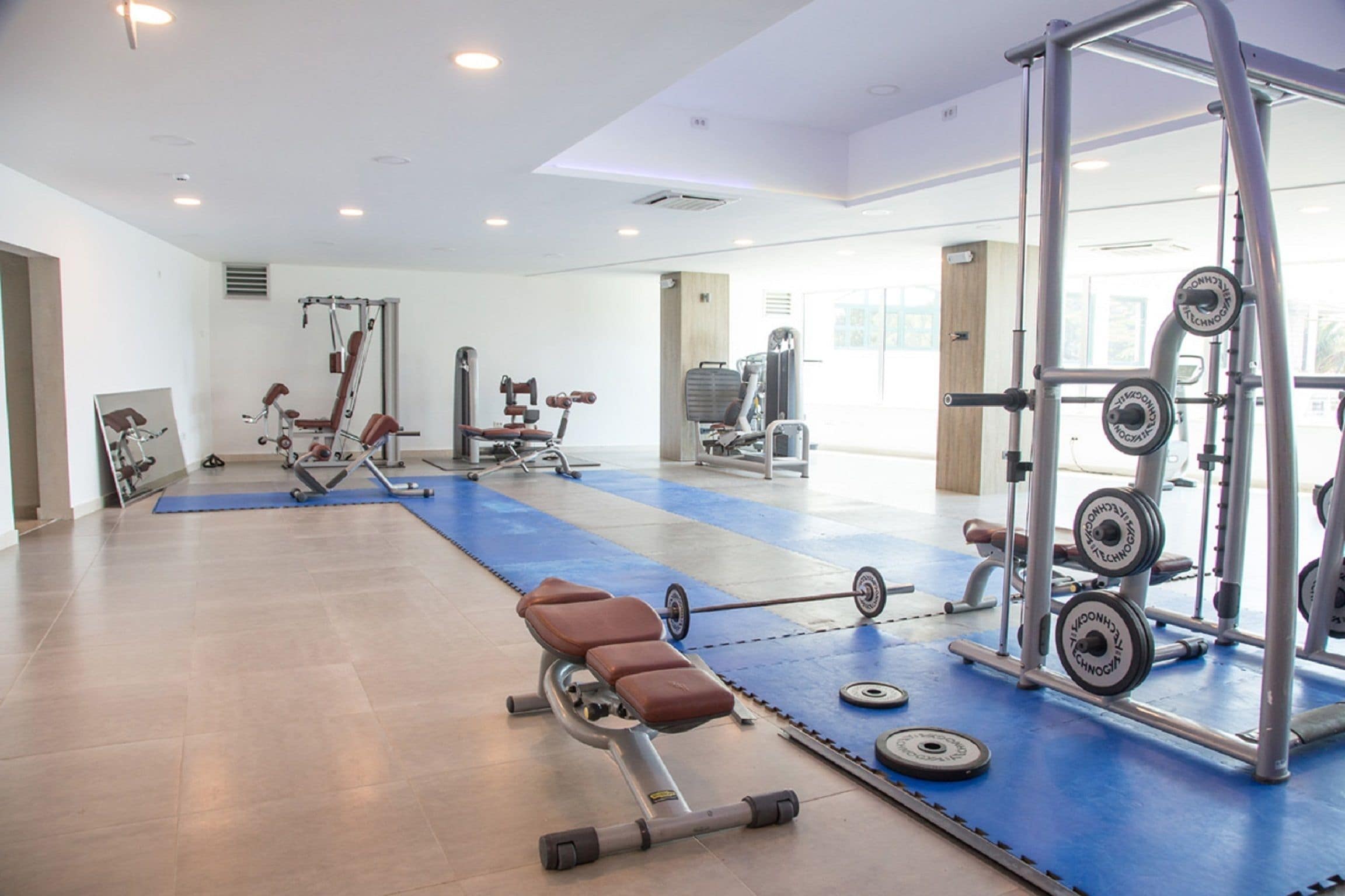 A gym with various exercise equipment, a blue mat area, and a weightlifting station.