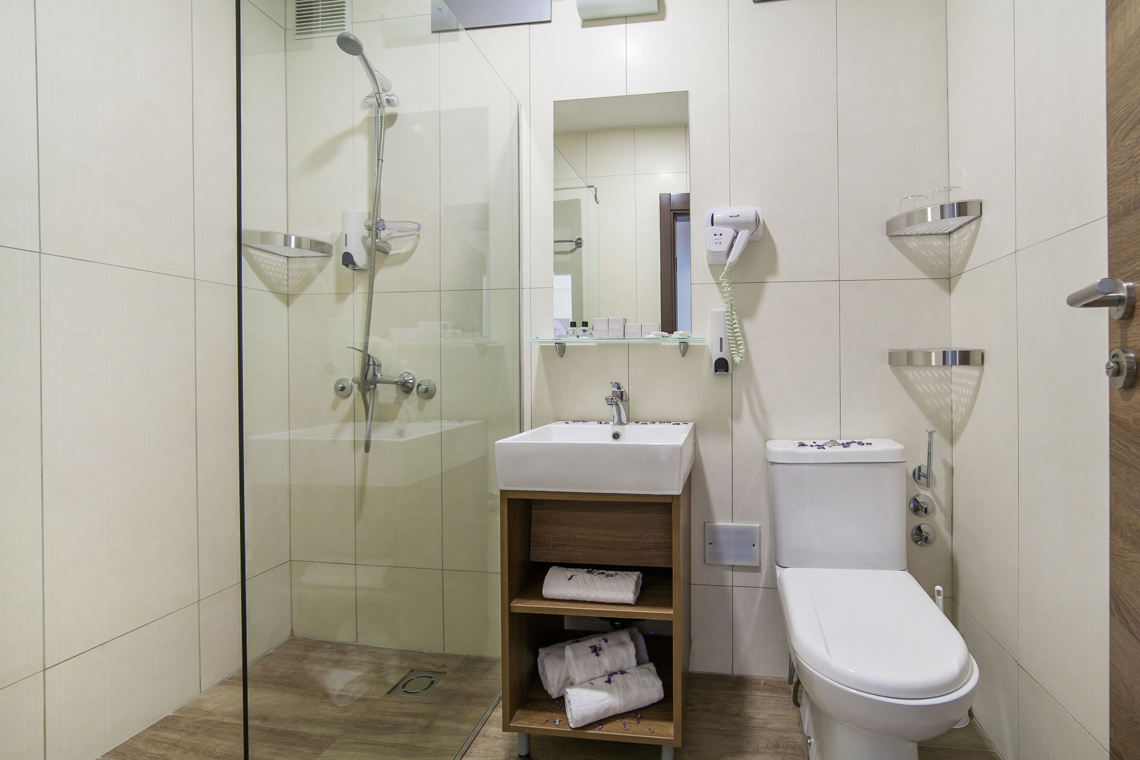 A modern bathroom with a glass-enclosed shower, a white sink with a wooden shelf, and a toilet.