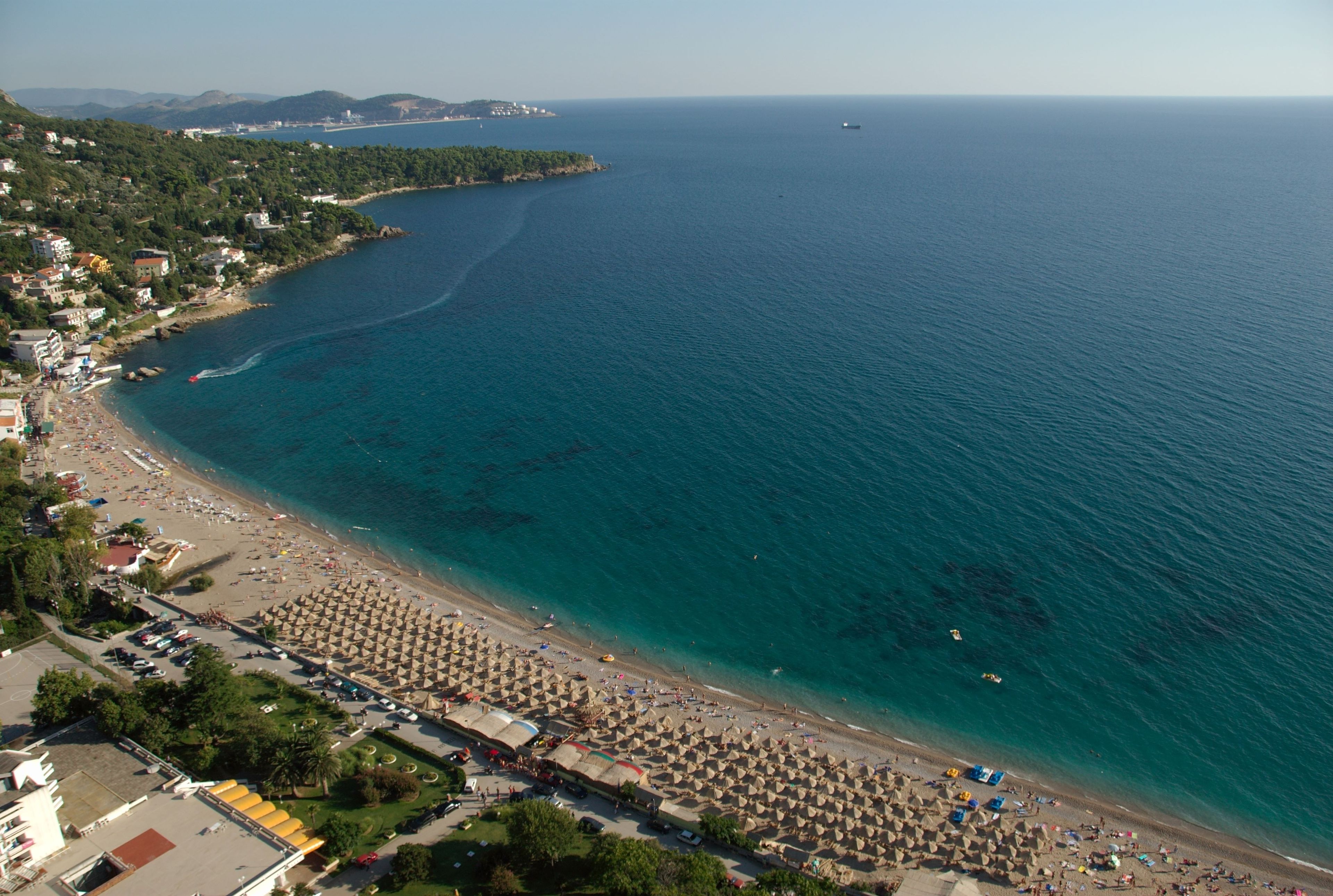 Ein Luftbild einer Küstenlandschaft mit Strand, Sonnenschirmen und Gebäuden.