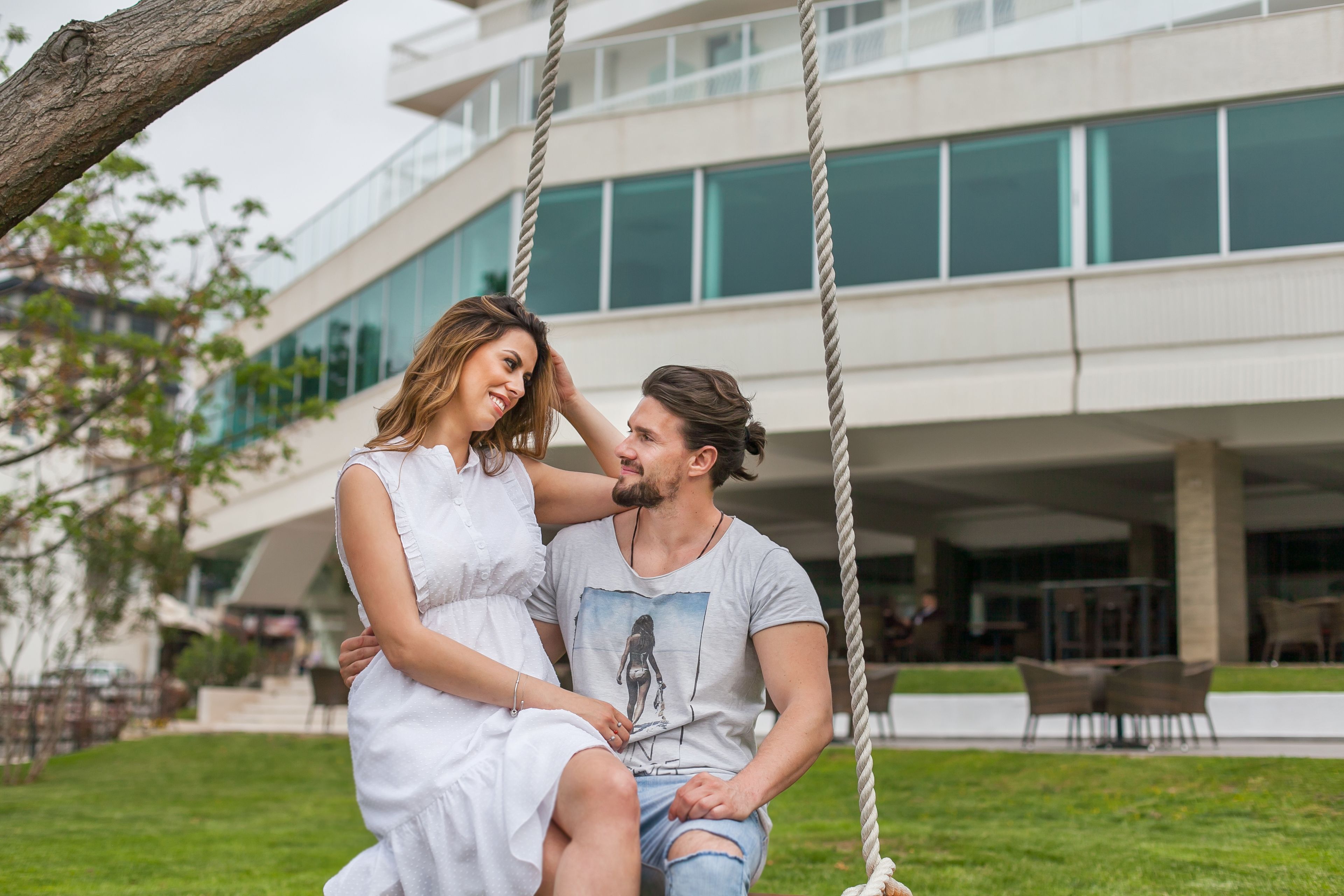 A couple sitting on a swing with a modern building in the background.
